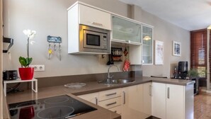 Une cuisine moderne avec des meubles blancs, un four à micro-ondes encastré, un évier en acier inoxydable et une plante en pot rouge.