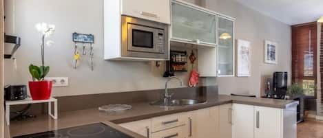 Cocina moderna con gabinetes blancos, un microondas integrado, un lavamanos de acero inoxidable y una planta roja en maceta.