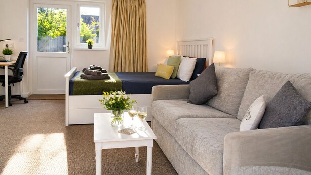 A cozy room with a bed, a sofa, a small table with drinks, a desk, and a window with curtains. - Lodge 7 - Lytton Tree Lodge, Reydon, Southwold (Reydon)