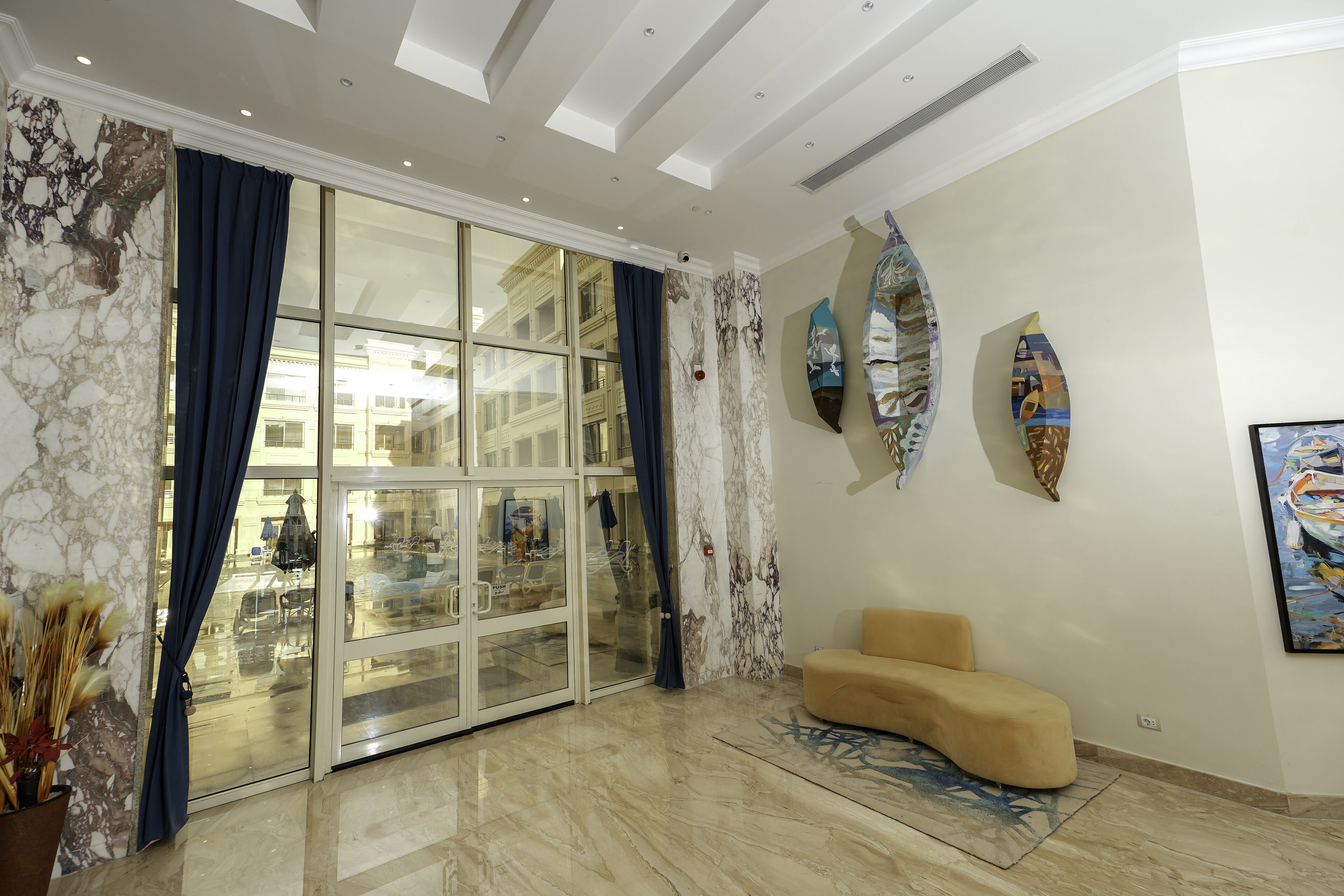 Un vestíbulo amplio con una gran puerta de vidrio, un sofá color beige y tres piezas de arte mural con forma de tabla de surf.