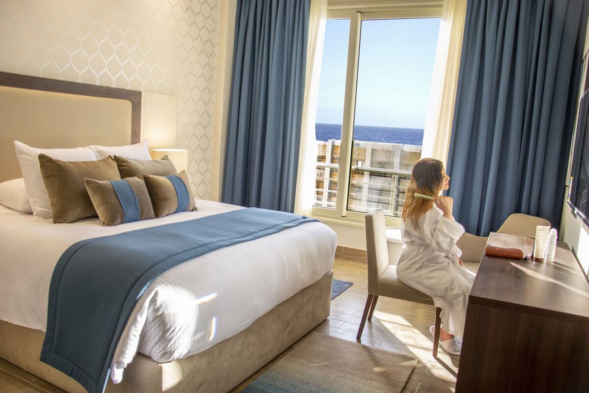 A hotel room with a large bed, a desk, and a view of the ocean.