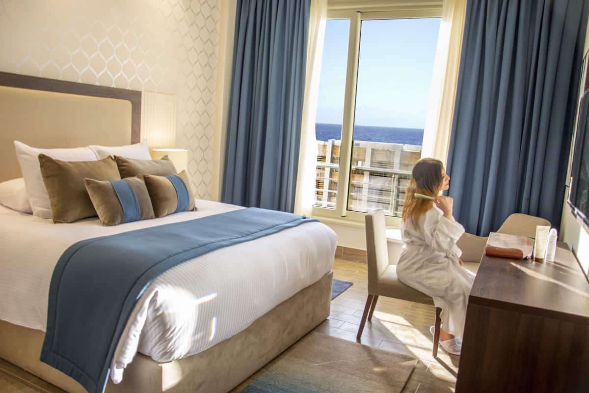 Ett hotellrum med en stor säng, ett skrivbord och utsikt över havet.