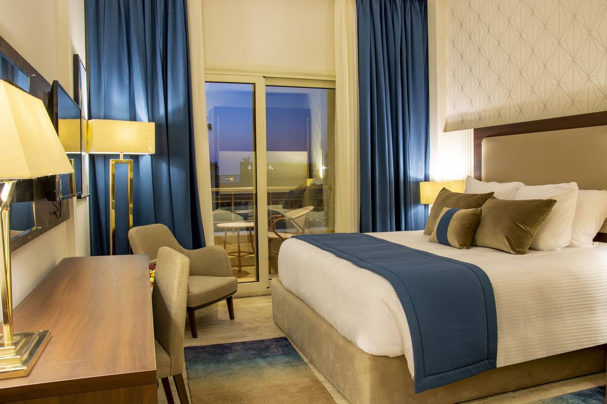 A hotel room with a bed, a desk, a chair, and a view of the outside.