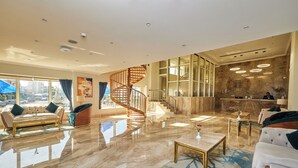 Eine geräumige Lobby mit Marmorboden, einer Wendeltreppe aus Holz und einer Sitzecke mit einer Couch und Sesseln.