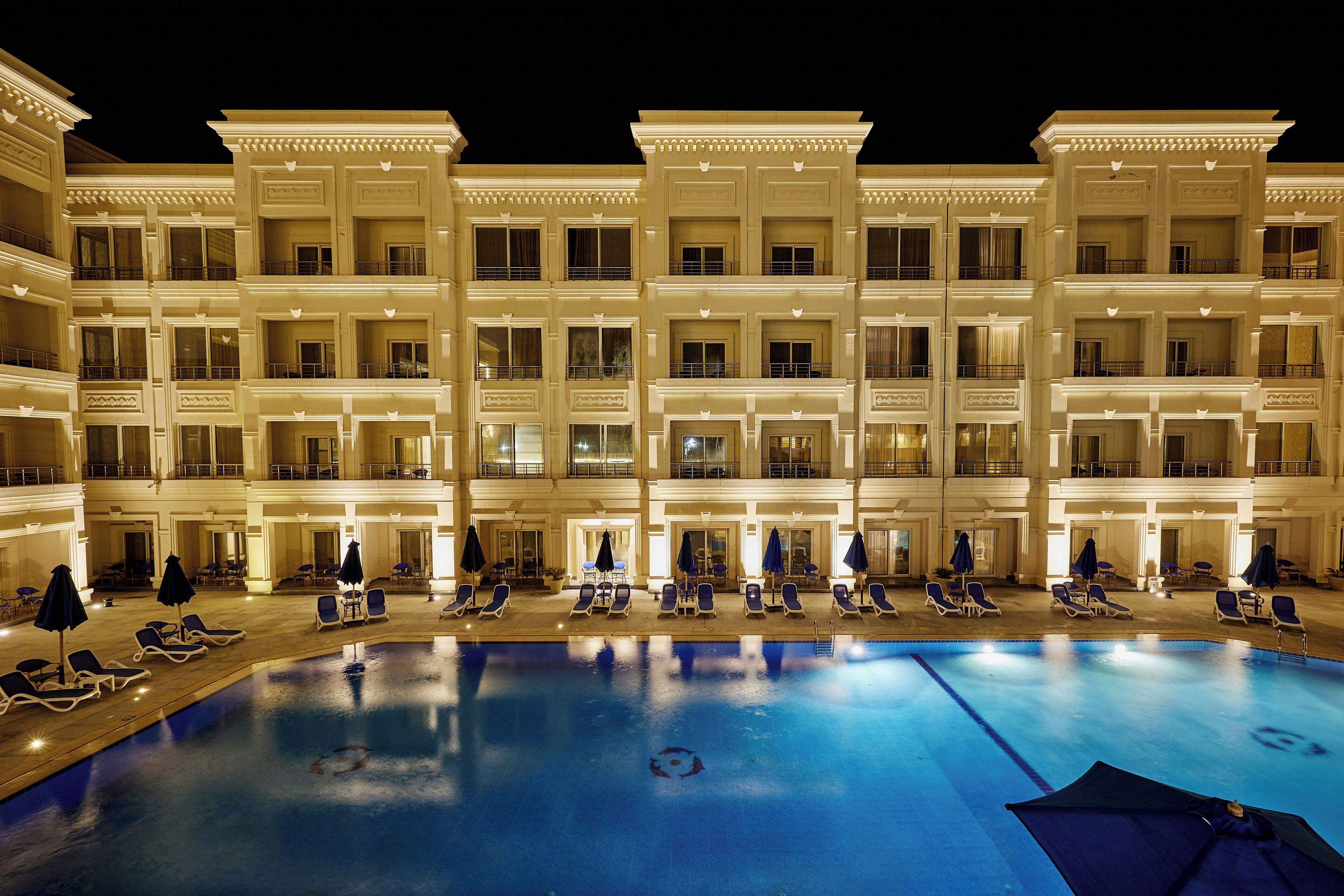 A multi-story hotel with a swimming pool, sun loungers, and umbrellas.