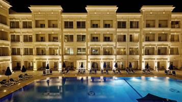 A multi-story hotel with a swimming pool, sun loungers, and umbrellas.