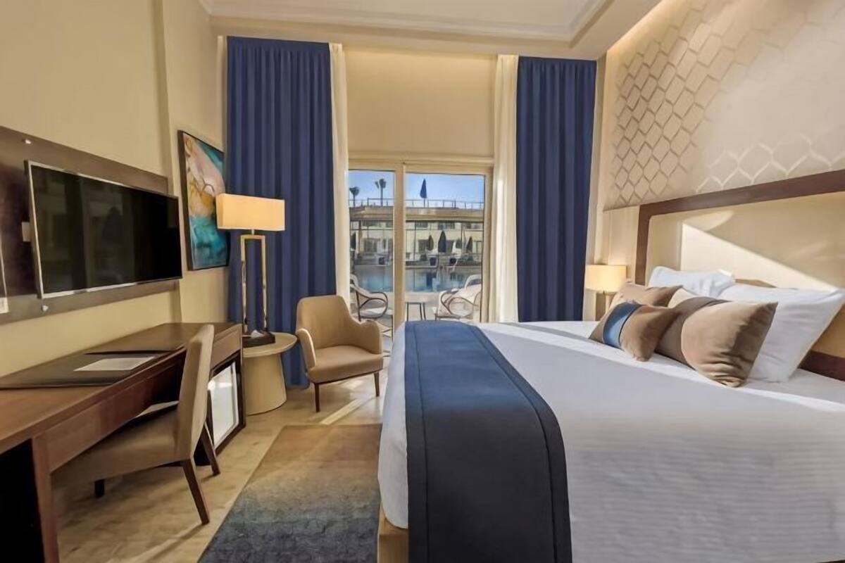 A hotel room with a bed, desk, chair, TV, and a balcony with a view.