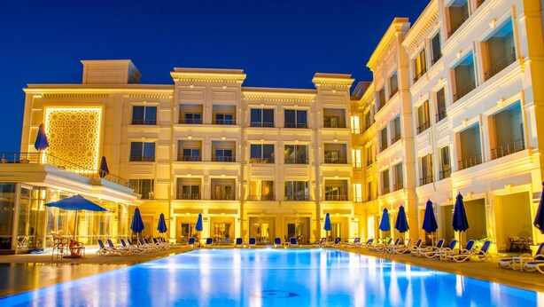 Ein großes, helles Hotel mit Schwimmbad, mehreren Balkonen und Liegestühlen.