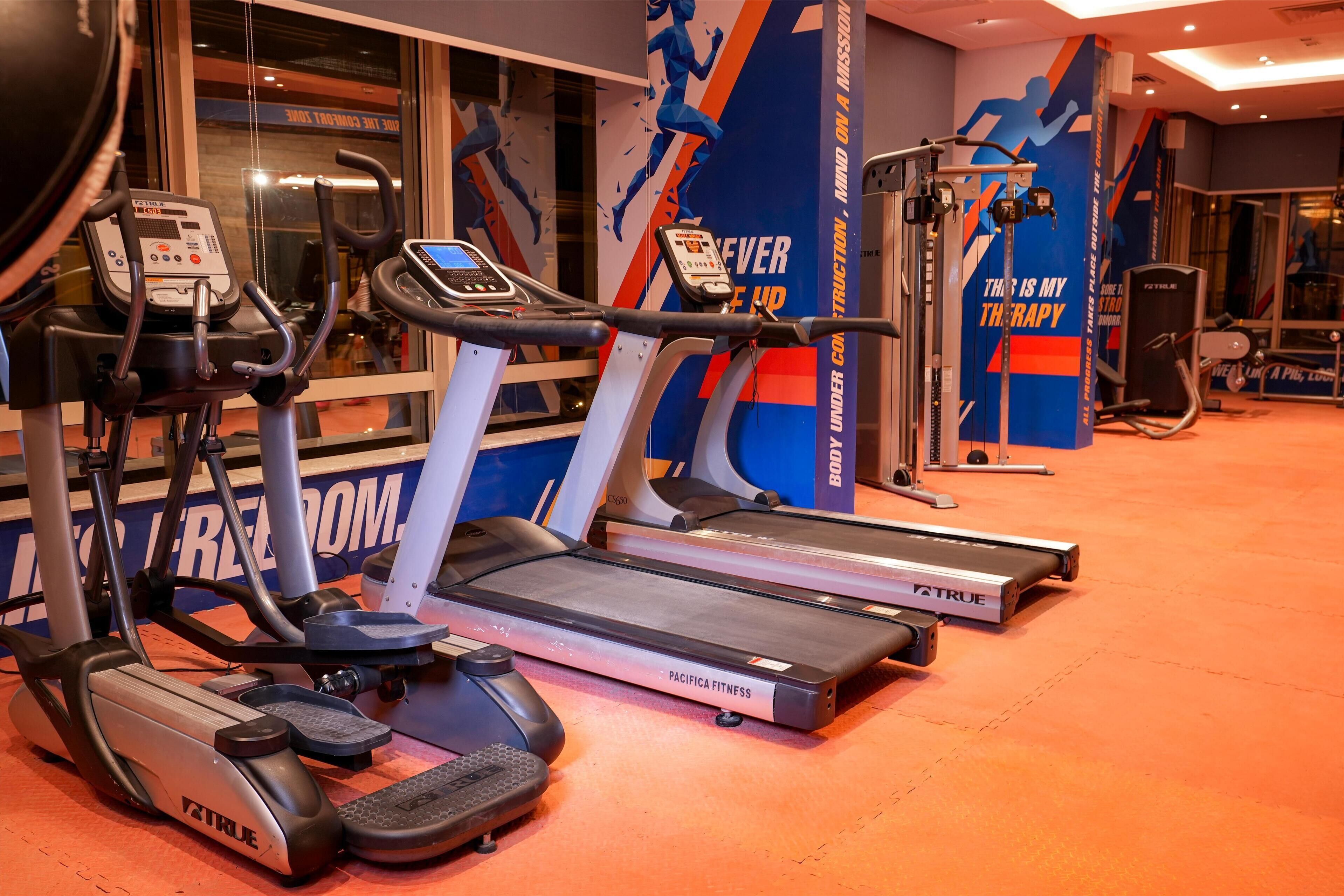 Une salle de sport équipée de tapis de course, d’un appareil elliptique et de machines de musculation.