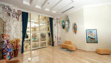 A spacious living area with a marble floor, a glass door leading to a balcony, and a wall adorned with surfboards and a framed painting.
