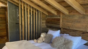 Een slaapkamer met een houten plafond, een bed met witte lakens, een zacht kussen en een teddybeer.