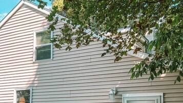Ein zweistöckiges Haus mit Eingangstür und kleiner Veranda, ein Baum spendet Schatten.