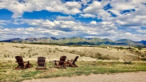 Three wooden Adirondack chairs in a desert landscape with mountains in the background. - BirdSong Desert Retreat: Reconnect. Rejuvenate. (Nogales)