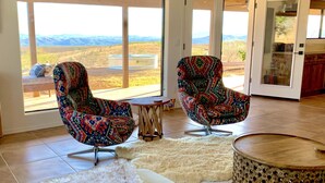 A modern living room with two patterned armchairs, a fluffy rug, and a round wooden table. - BirdSong Desert Retreat: Reconnect. Rejuvenate. (Nogales)