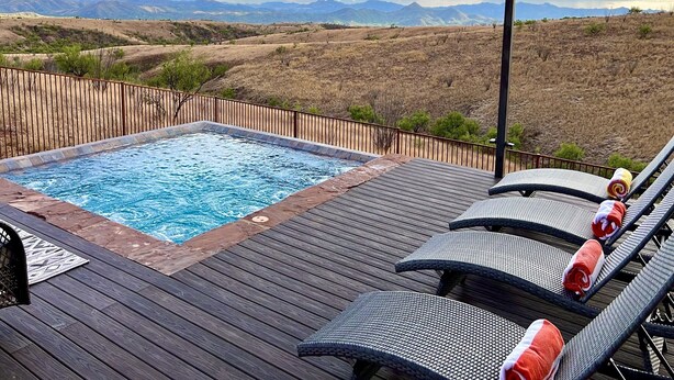 A hot tub on a wooden deck with lounge chairs, surrounded by a fence and a view of mountains. - BirdSong Desert Retreat: Reconnect. Rejuvenate. (Nogales)