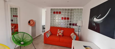 A modern living room with a red sofa, green and yellow chairs, a glass block wall, and a large painting.