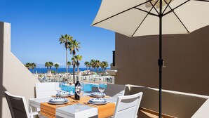 A dining table with white chairs and a beige umbrella, overlooking a pool and palm trees. - Apartment El Faro for 3 people in the south of Tenerife (Palm-Mar)