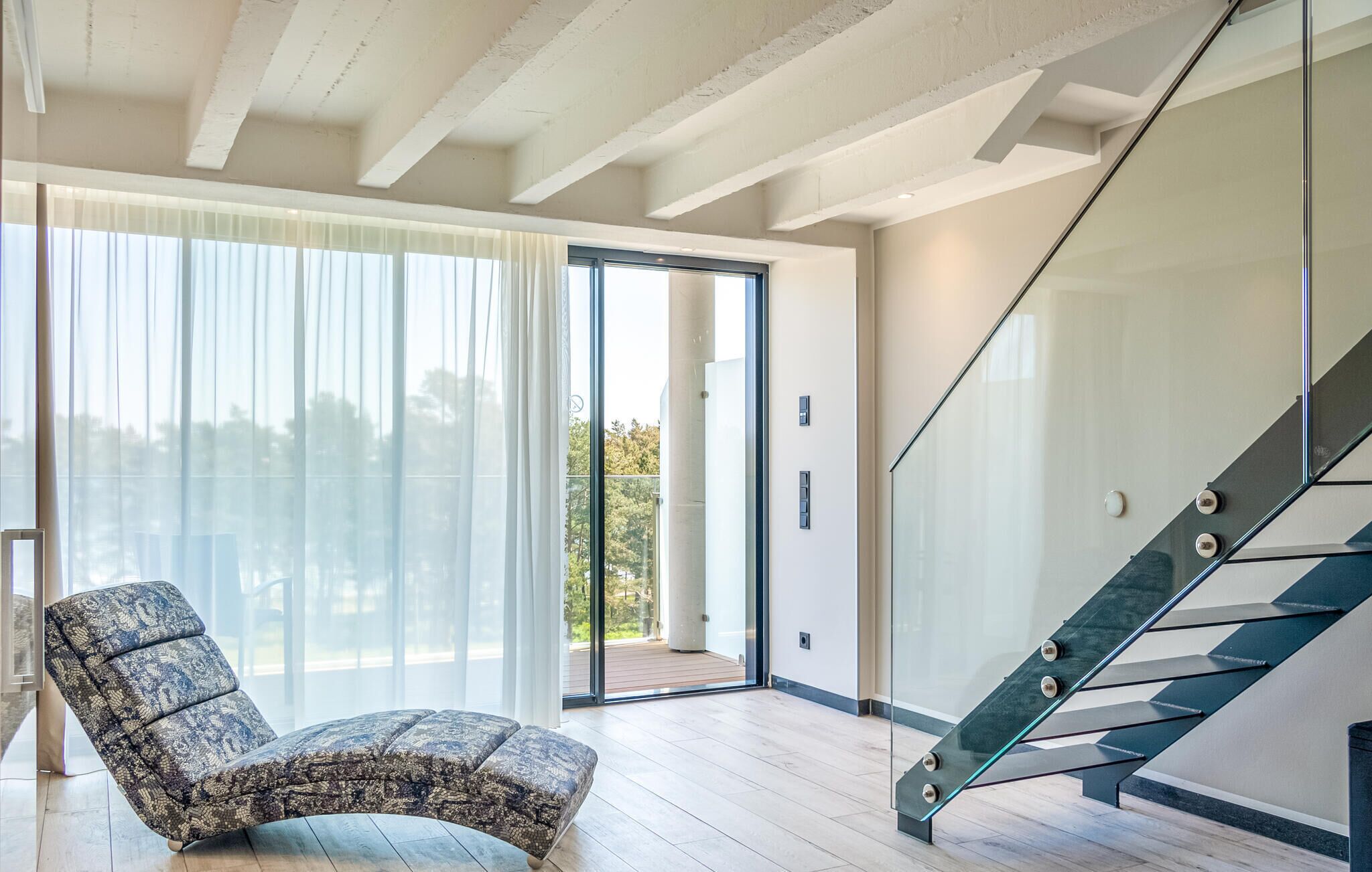 A modern interior with a glass staircase, a patterned ottoman, and a large sliding glass door leading to an outdoor area.