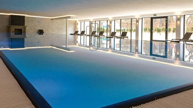 An indoor swimming pool with clear glass walls, lounge chairs, and a view of the outdoors. - Stunning apartment in Binz (Binz)