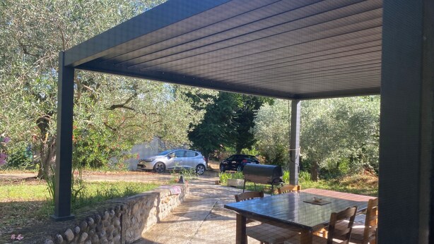 Un espacio al aire libre cubierto con un muro de piedra, una mesa con sillas y un coche estacionado afuera.