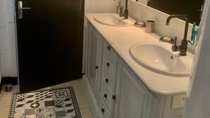 Un baño con dos lavamanos, una puerta oscura, una alfombra estampada y un espejo sobre los lavamanos.