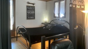 Una habitación pequeña y acogedora con una cama individual, una silla, una mesita de noche y una lámpara fijada a la pared.