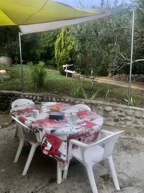 Un patio al aire libre con una mesa preparada para cuatro personas, cubierto por un paraguas amarillo.