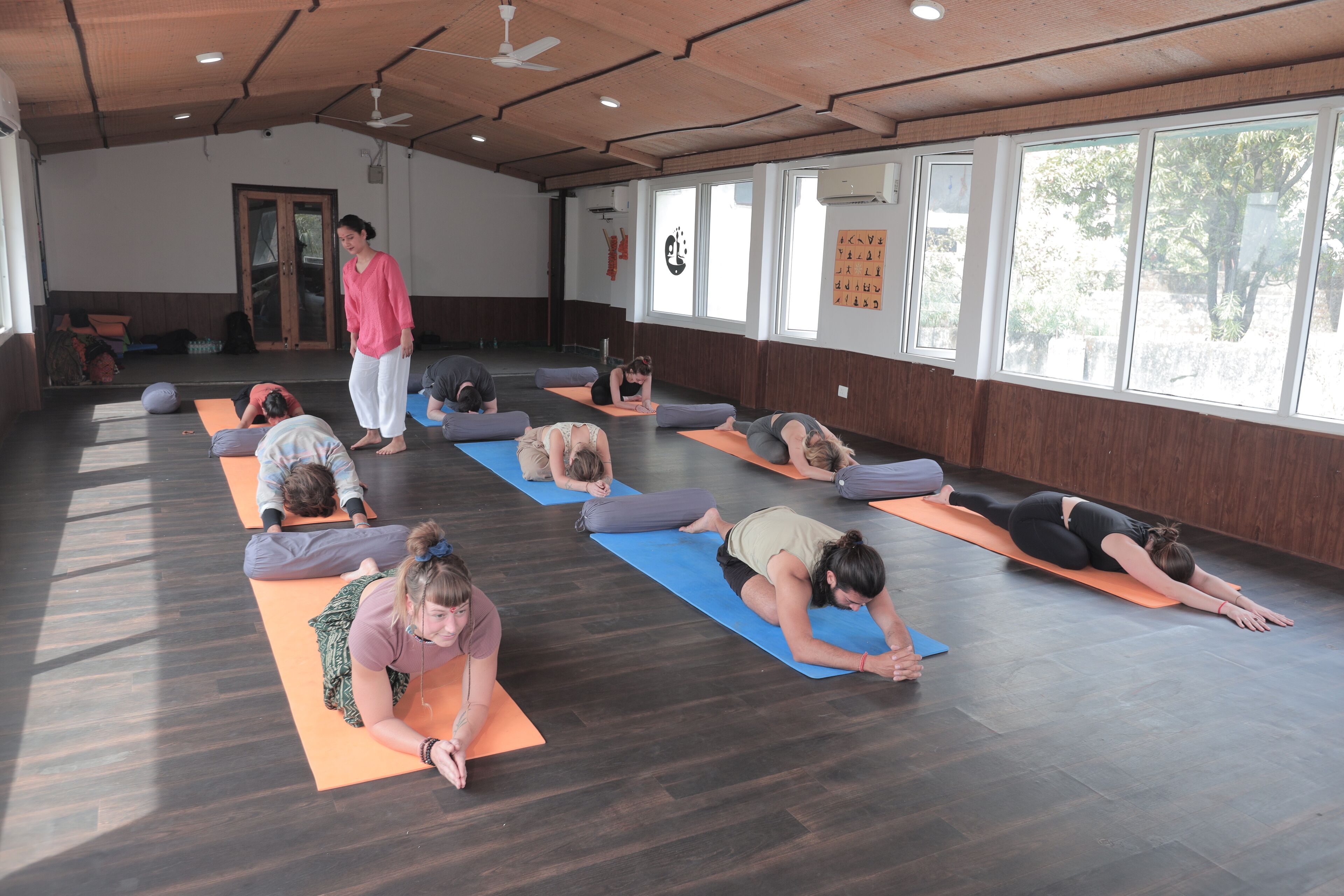 A yoga class in a room with wooden floors, large windows, and a ceiling fan.