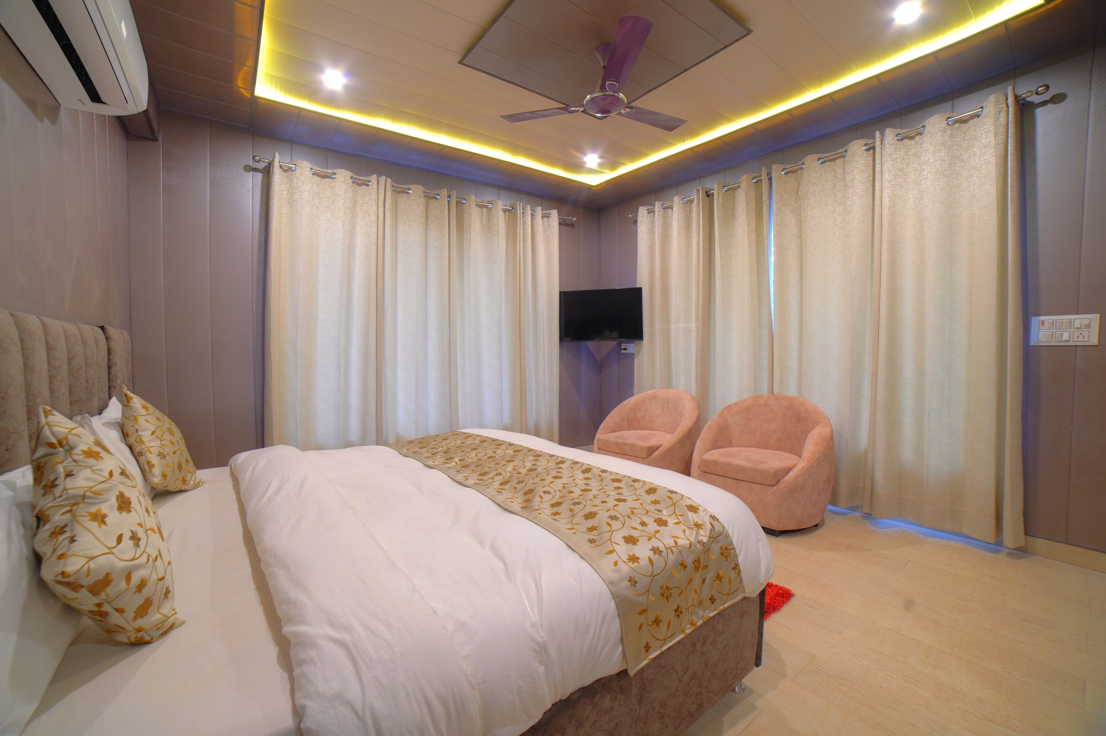 A bedroom with a bed, two chairs, a ceiling fan, and a TV.