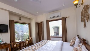 A hotel room with a bed, a desk, a chair, a television, and a window with curtains. - Yogved Hospitality And Resort (Narendranagar)