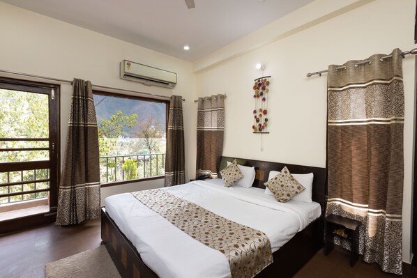 A hotel room with a large bed, a nightstand, an air conditioning unit, and a view of the outdoors. - Yogved Hospitality And Resort (Narendranagar)
