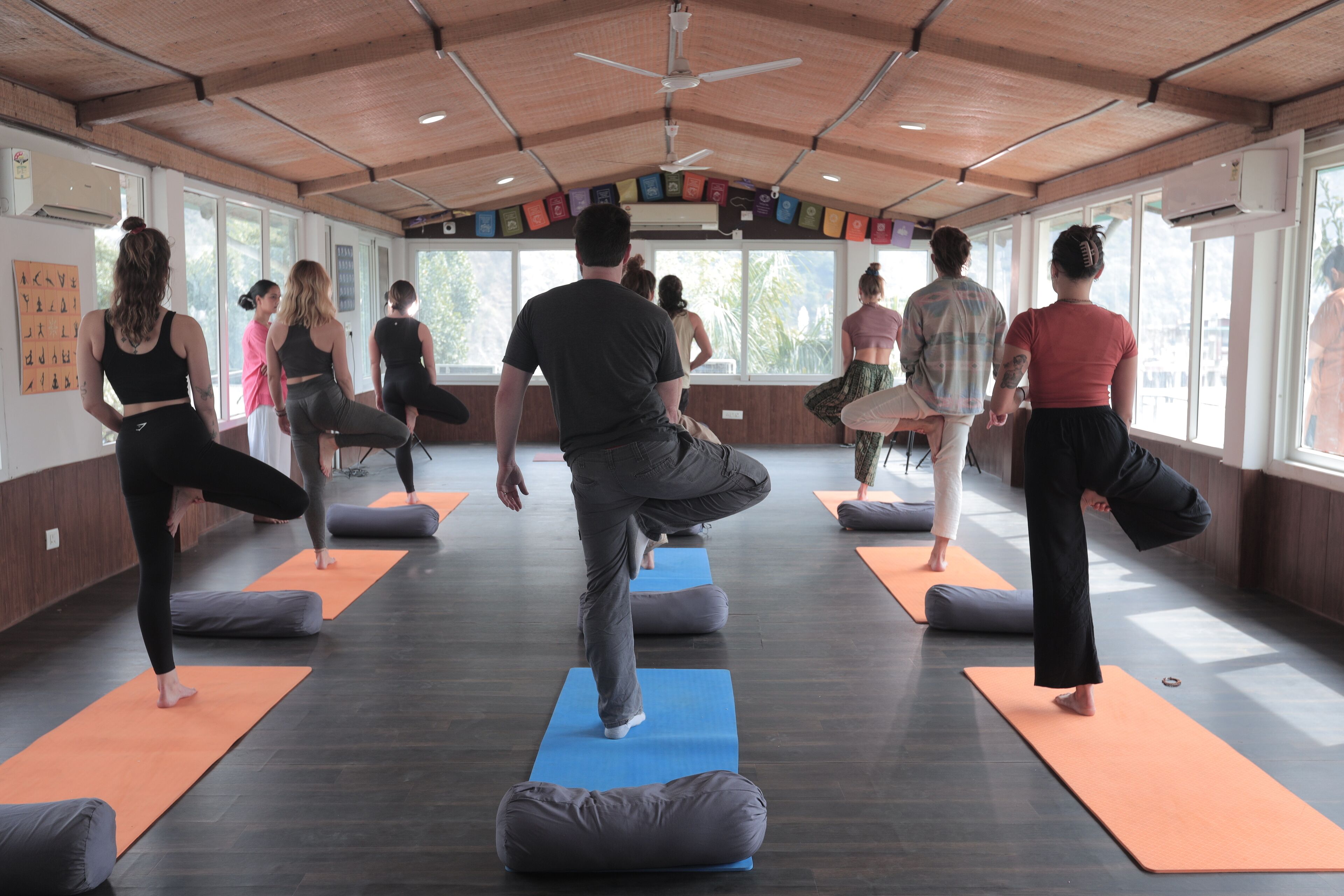 A yoga class in a room with large windows, wooden ceiling, and mats on the floor.