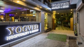 Het uiterlijk van YOGVED Hospitality & Resort met een goed verlichte ingang, een zichtbaar receptiebalie en een pad dat naar het hoofdgebouw leidt.