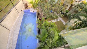 A swimming pool with a blue mosaic design, surrounded by lush greenery and palm trees. - Yogved Hospitality And Resort (Narendranagar)