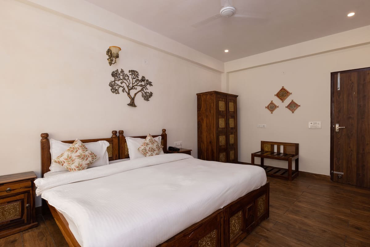 A neatly arranged bedroom with a large bed, a wooden cabinet, a small table, and a door.