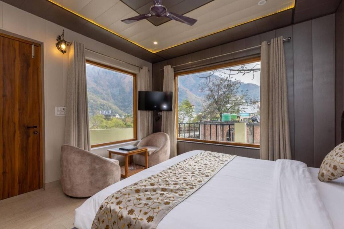A hotel room with a bed, a desk, a chair, a television, and large windows with a mountain view.