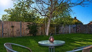 A backyard with a round table, two chairs, a decorative vase, and a wooden fence. - Lodge 5 - Lytton Tree Lodge, Reydon, Southwold (Reydon)