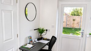 A room with a desk, chair, a potted plant, a mirror, and a door leading to a backyard. - Lodge 5 - Lytton Tree Lodge, Reydon, Southwold (Reydon)