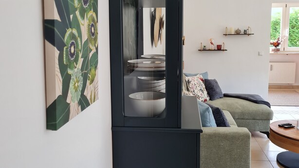 A modern living room with a black cabinet, a green sofa, and a large mirror reflecting the room. - Central in August 2022 newly renovated apartment Katja II with Kramerblick (Garmisch-Partenkirchen)