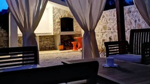 An outdoor patio area with a stone wall, a fireplace, and a seating area with tables and chairs. - Holiday House Galeb - 20 meters from Beach! (Sevid)