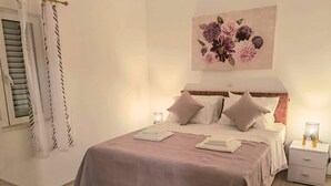 A neatly made bed with a pink bedspread, two bedside lamps, and a floral artwork above the bed. - Holiday House Galeb - 20 meters from Beach! (Sevid)