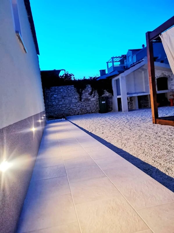 A paved pathway leading to a building with stone walls and a tiled floor.