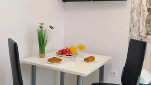 A dining area with a white table, two black chairs, a television above the table, and a small plant on the table. - Holiday House Galeb - 20 meters from Beach! (Sevid)