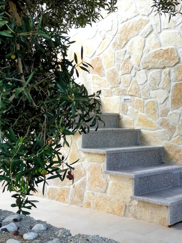 A stone staircase leading up to a door, surrounded by a stone wall and greenery.