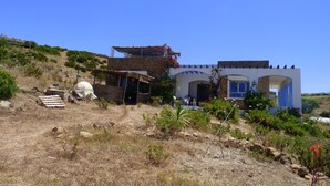 A rustic building with a stone facade, a thatched roof structure, and a small garden with potted plants. - DAR CLARA, or DAR FKRUN (Double room) (Arcila-Mejlaw)