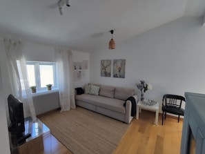 Un salon avec un canapé, une petite table, une chaise, un radiateur et une fenêtre avec des rideaux.