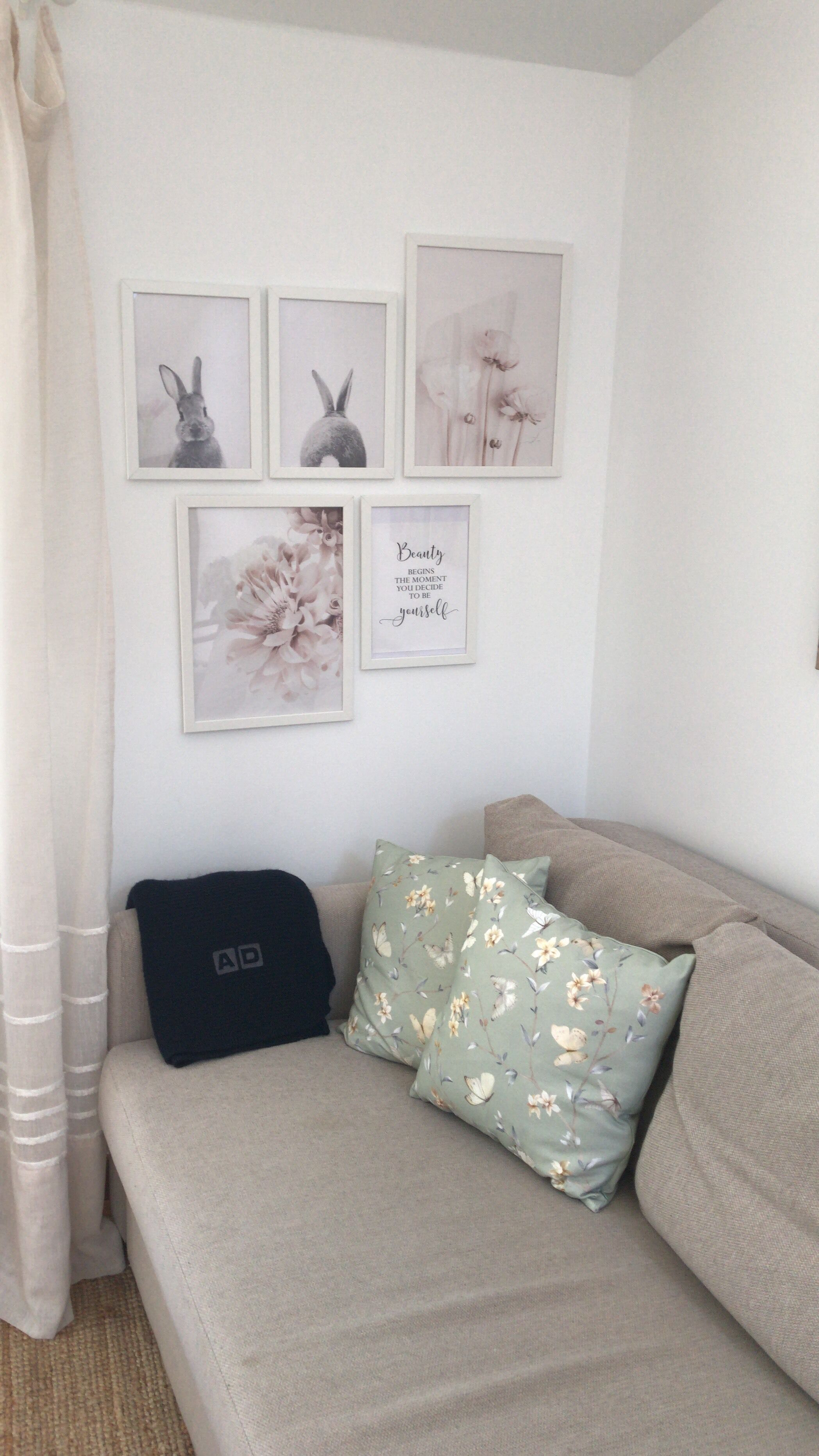 Una sala de estar acogedora con un sofá color beige, dos cojines y cuatro cuadros en la pared.