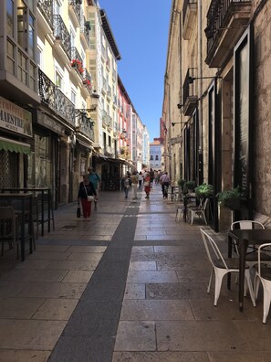 Une rue étroite bordée de cafés et de boutiques, avec des terrasses et un trottoir réservé aux piétons.