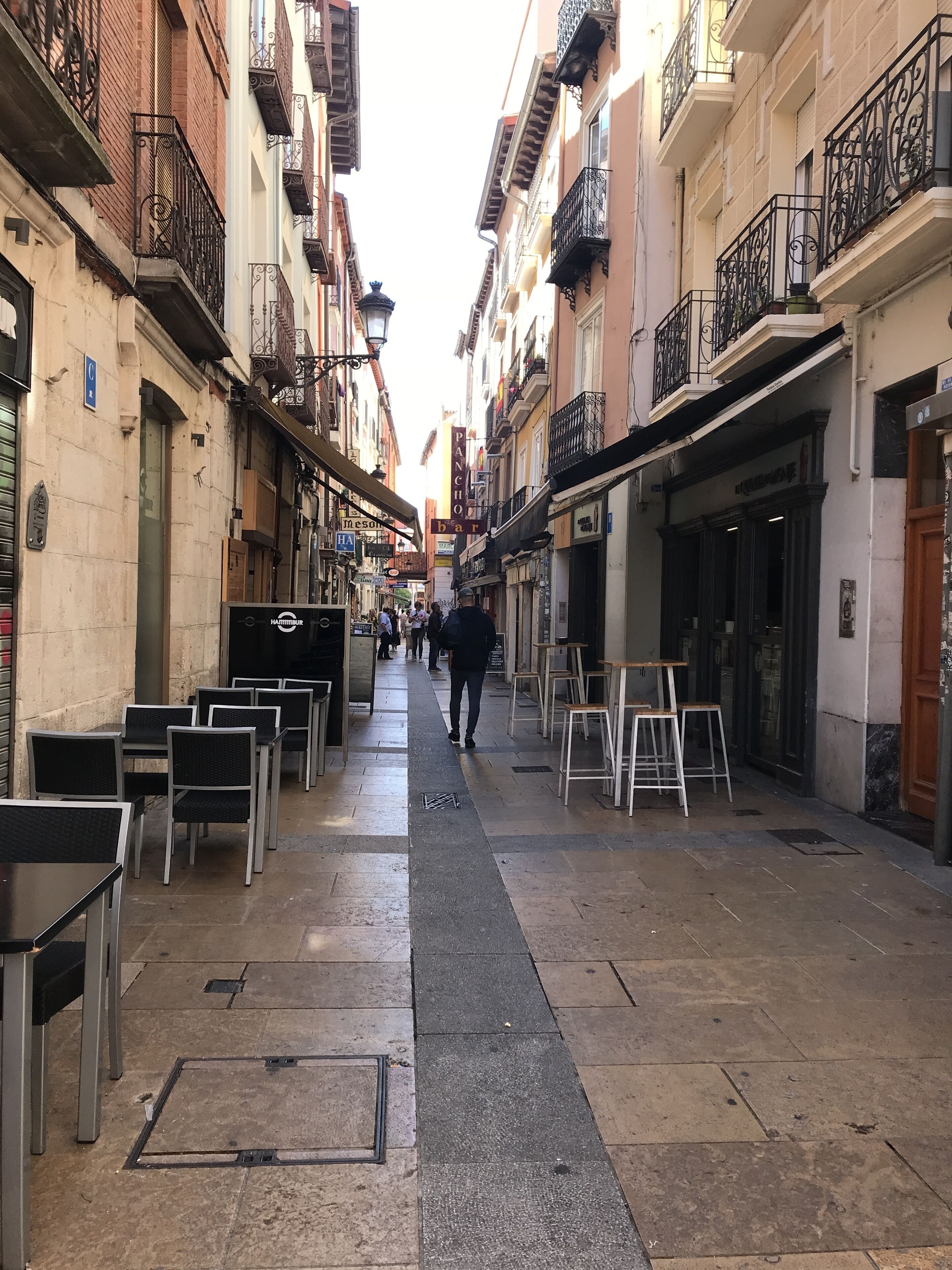 A narrow street lined with buildings, some with balconies and outdoor seating.