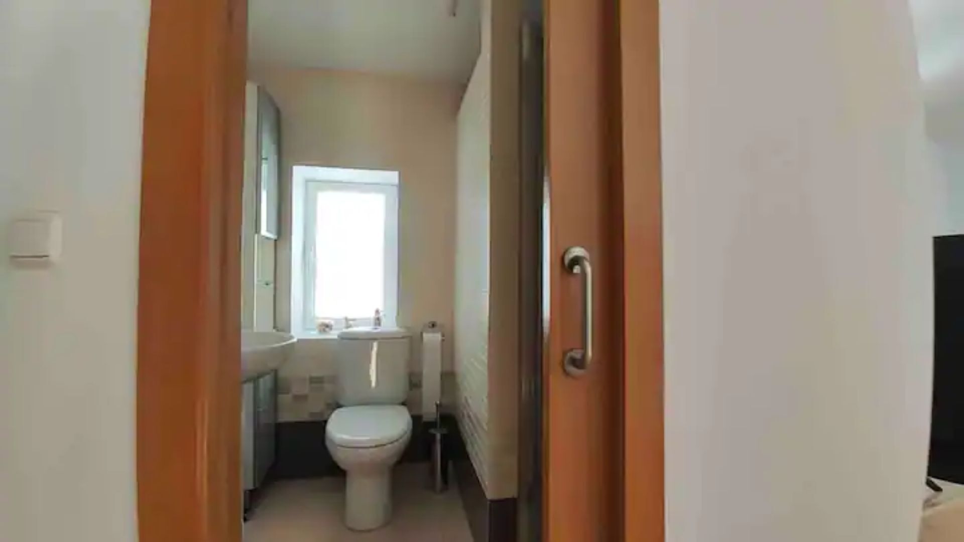 Un pasillo estrecho que da a un baño con inodoro, lavamanos y espejo.